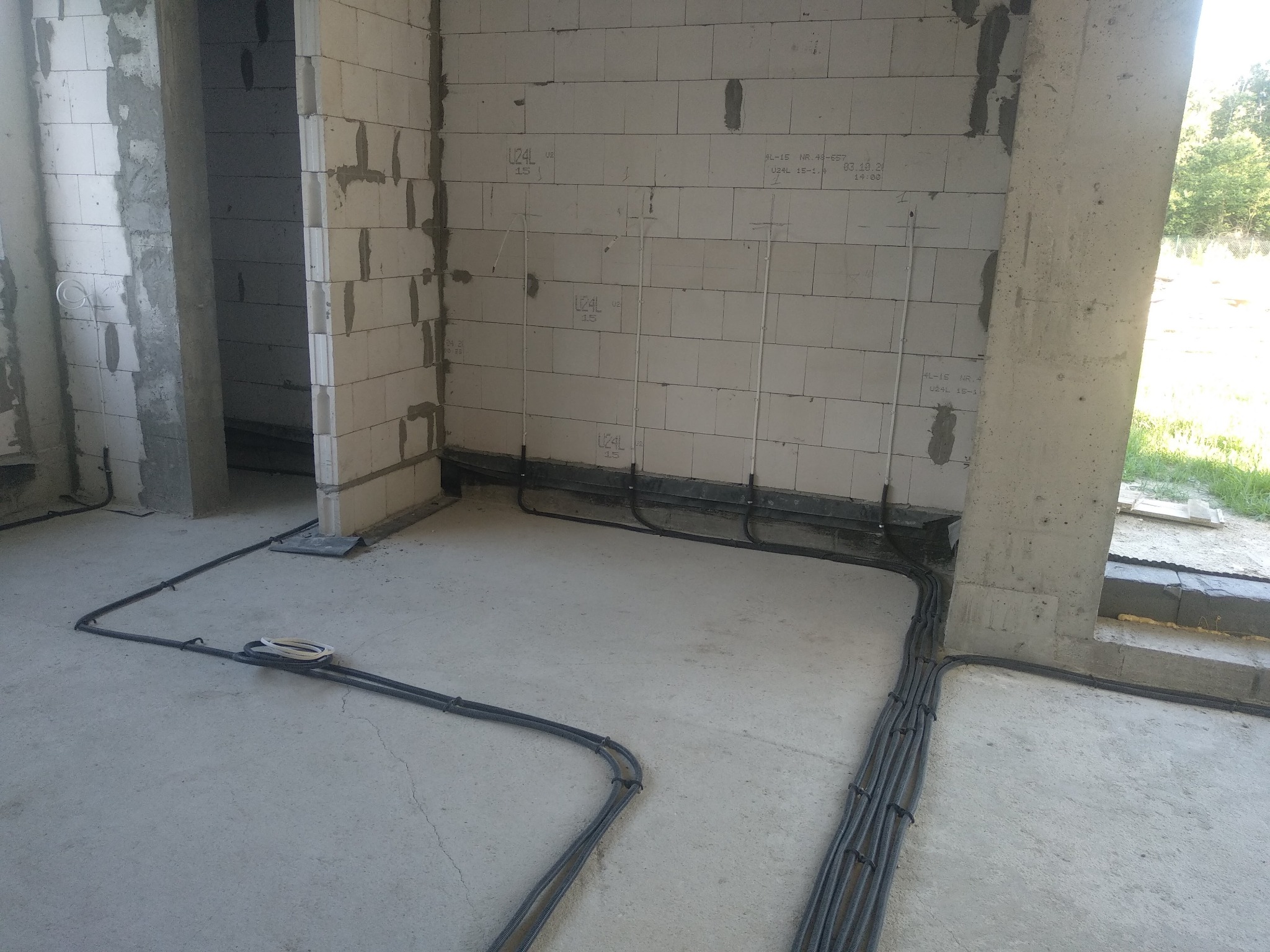 Surowe wnętrze w trakcie prac instalacyjnych: widoczne kable elektryczne prowadzone po podłodze wzdłuż ścian z betonu komórkowego, przygotowane do dalszej instalacji. Na ścianach zaznaczone punkty...