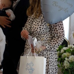 Magdalena Pawlak - Uśmiechnięta kobieta z prezentami i balonem 'Chrzest Święty Boryska', obok mężczyzna z dzieckiem. Pamiątka Chrztu Świętego na torbie.