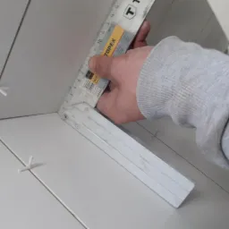 Układanie białych płytek z użyciem krzyżyków dystansowych i kątownika TOPE X, widok z bliska na fugi.