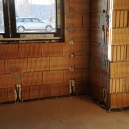 Electric Gods - Wewnętrzne ściany z cegły ceramicznej z przygotowanymi bruzdami i peszlami pod instalację elektryczną, widoczne puszki elektryczne i przewody przy podłodze.