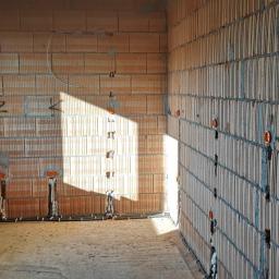 Electric Gods - Wnętrze w trakcie budowy z widocznymi przewodami elektrycznymi w ścianach z cegły ceramicznej, puszki instalacyjne zamontowane, przewody ułożone w korytach podłogowych, karton z elementami...