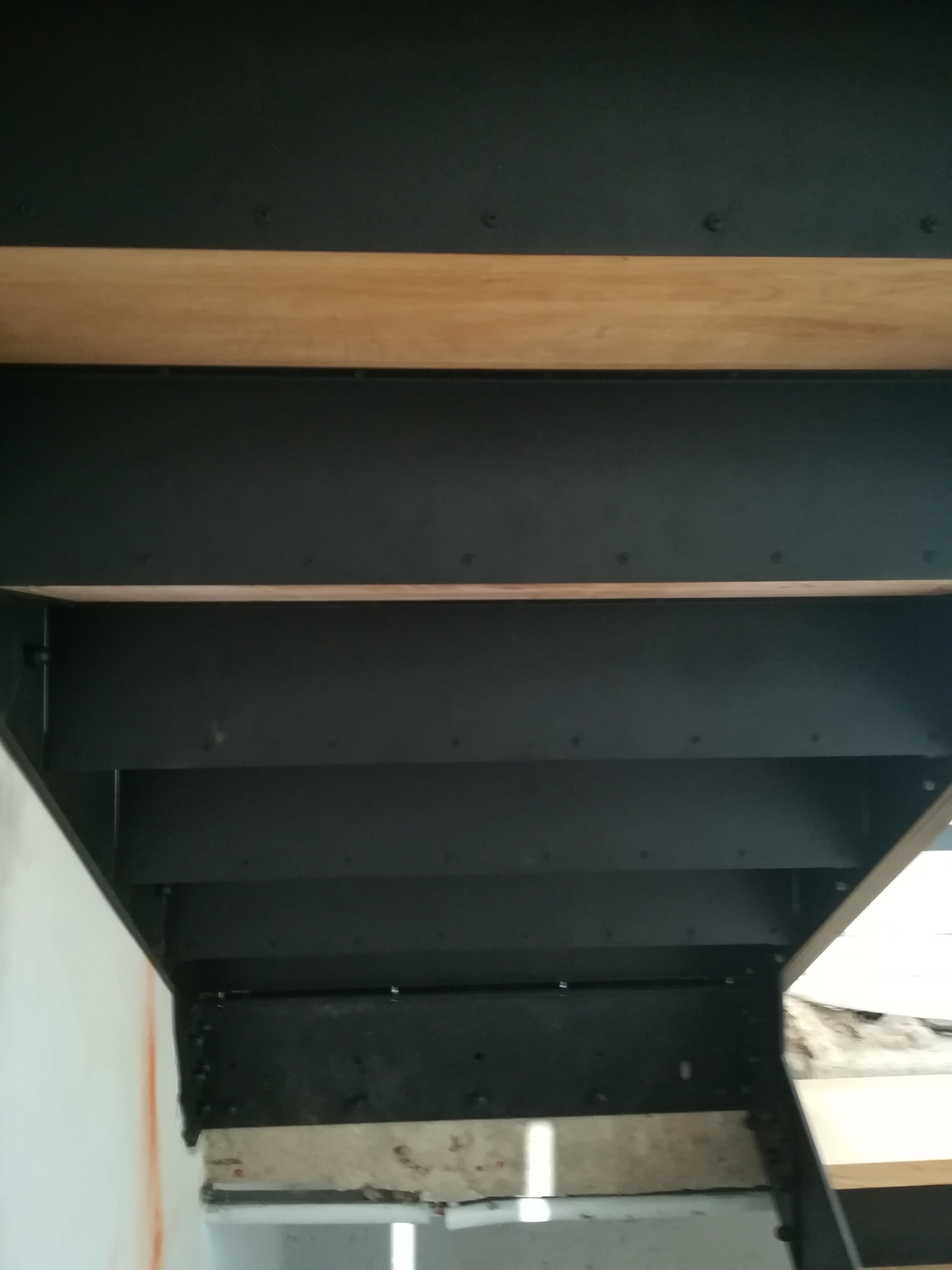 Metalowe schody z drewnianymi stopniami widziane od spodu, mocowane do ściany, widoczne ślady po montażu.