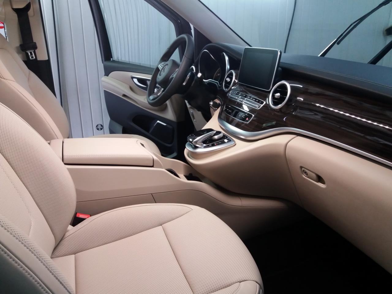 Wnętrze luksusowego vana Mercedes-Benz z beżową skórzaną tapicerką foteli, drewnianym wykończeniem deski rozdzielczej i nowoczesnym systemem sterowania.