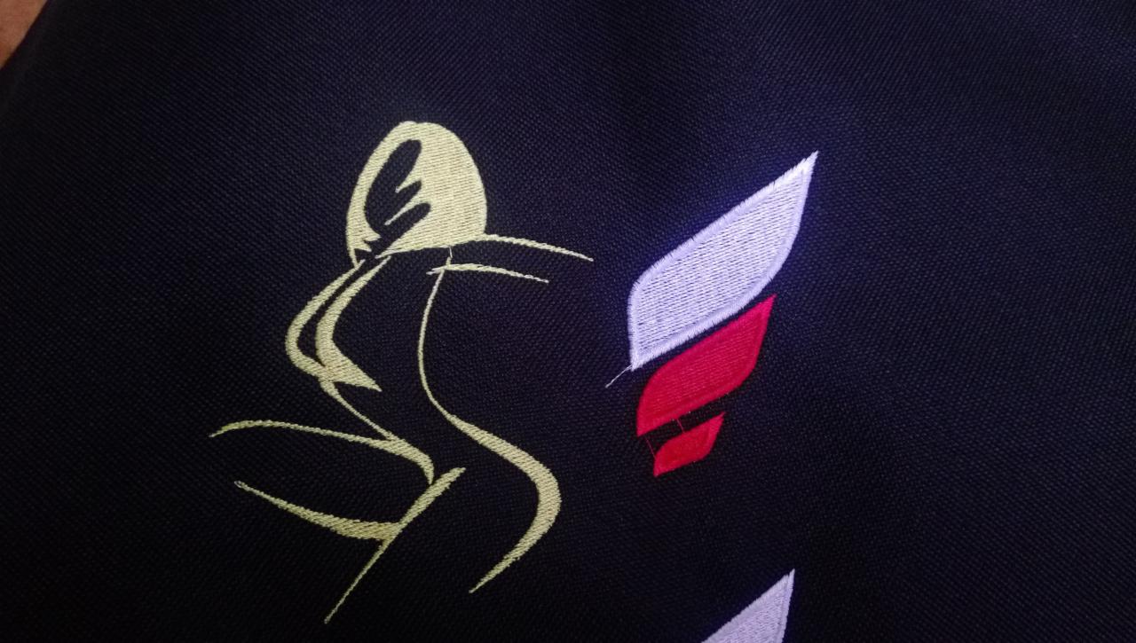 Czarna tkanina z wyhaftowanym stylizowanym motywem kobiety i elementami w kolorach białym i czerwonym.