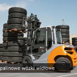 Wózek widłowy marki STILL transportuje paletę z oponami na tle stosów opon i żurawia budowlanego w oddali.