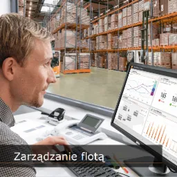 Mężczyzna analizuje dane dotyczące floty wózków widłowych na monitorze, widoczne wykresy i statystyki, w tle magazyn z wózkami widłowymi.