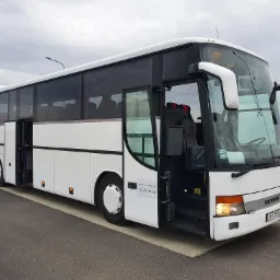 Biały autokar Setra z otwartymi drzwiami, zaparkowany na poboczu drogi, z widocznym numerem telefonu kontaktowego na boku pojazdu.