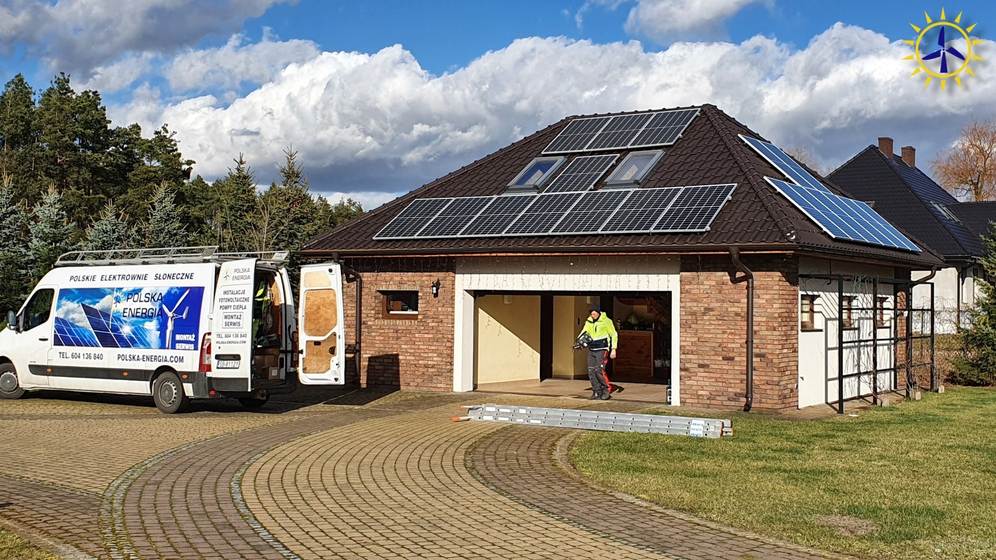 Montaż paneli fotowoltaicznych na dachu domu jednorodzinnego z widocznym samochodem firmy Polska Energia i pracownikiem wychodzącym z garażu, drabina oparta o budynek.