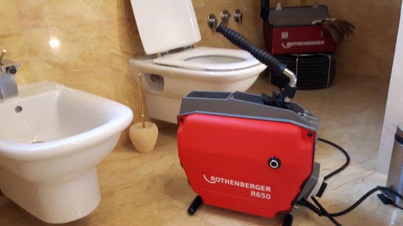 Czerwona maszyna Rothenberger R650 do udrażniania rur kanalizacyjnych w łazience z marmurowymi ścianami, widoczny bidet i toaleta.