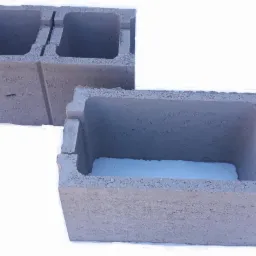 Dwa szare bloczki betonowe z otworami, jeden z nich ustawiony pionowo, drugi z dwoma otworami z góry, na białym tle.