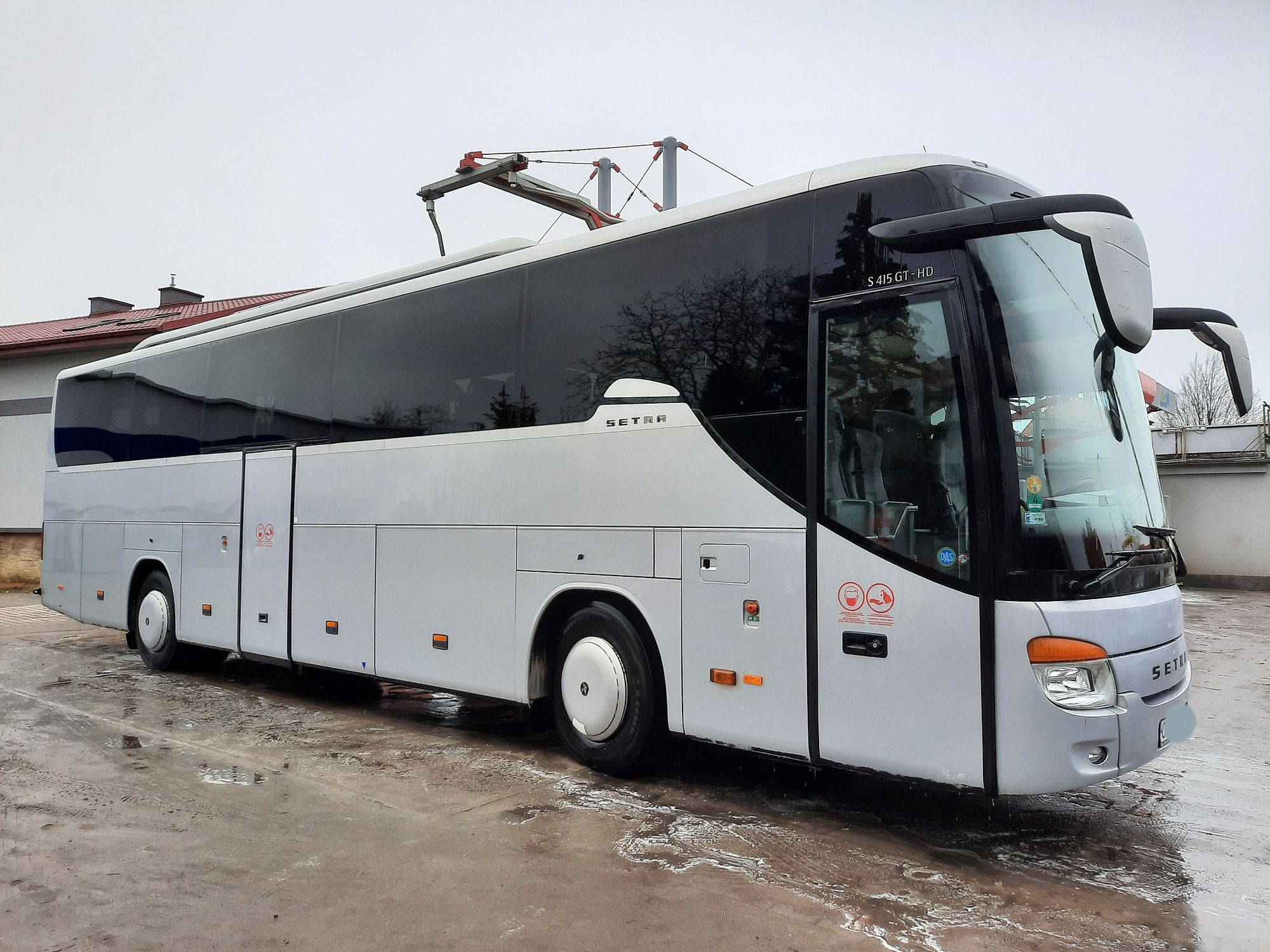 Biały autokar Setra S 415 GT-HD zaparkowany na mokrym placu przed budynkiem, widoczne detale nadwozia i osprzęt dachowy.
