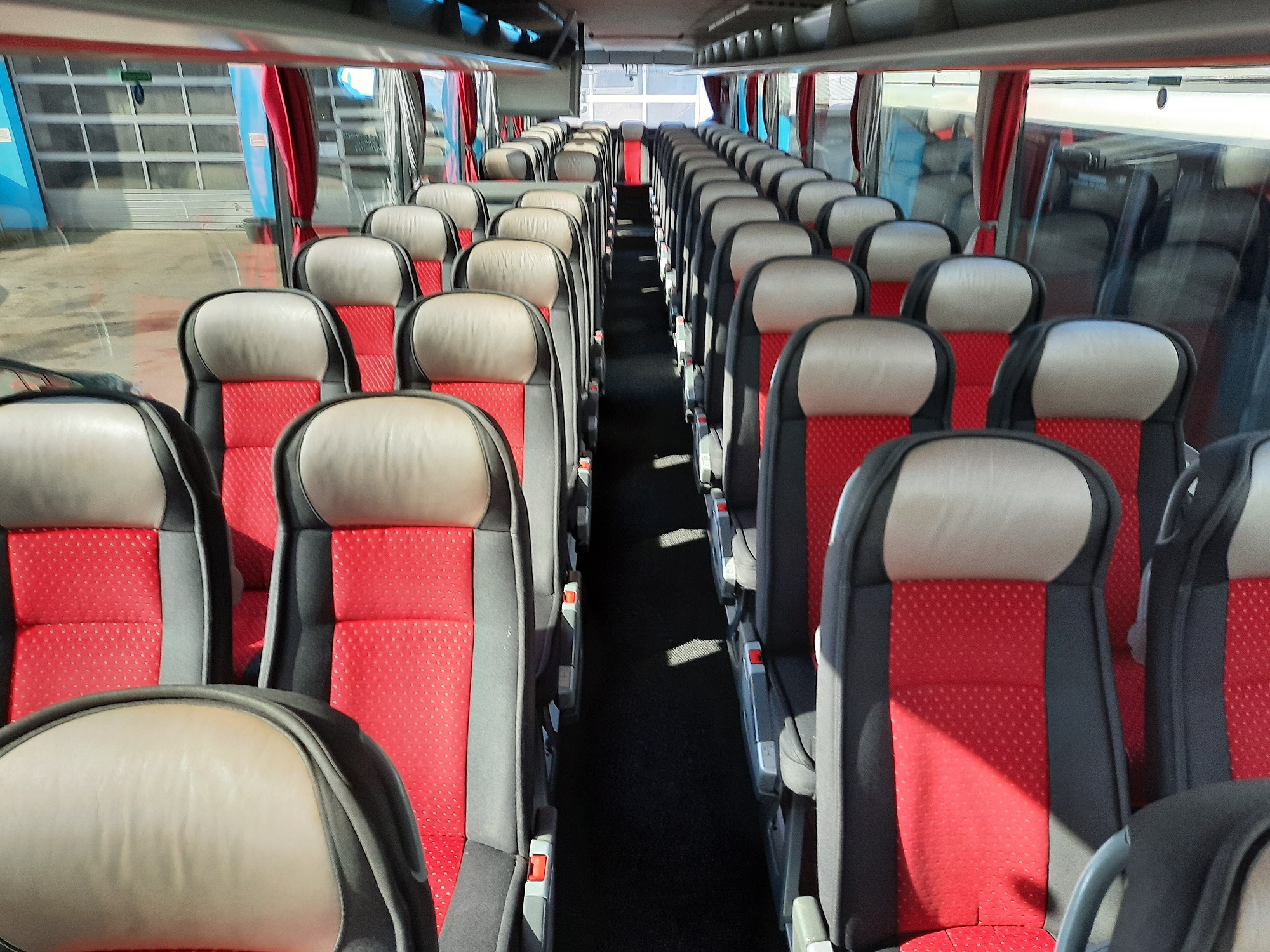 Wnętrze autobusu z rzędami czerwonych i szarych foteli, widok z przodu na puste siedzenia i okna po bokach.