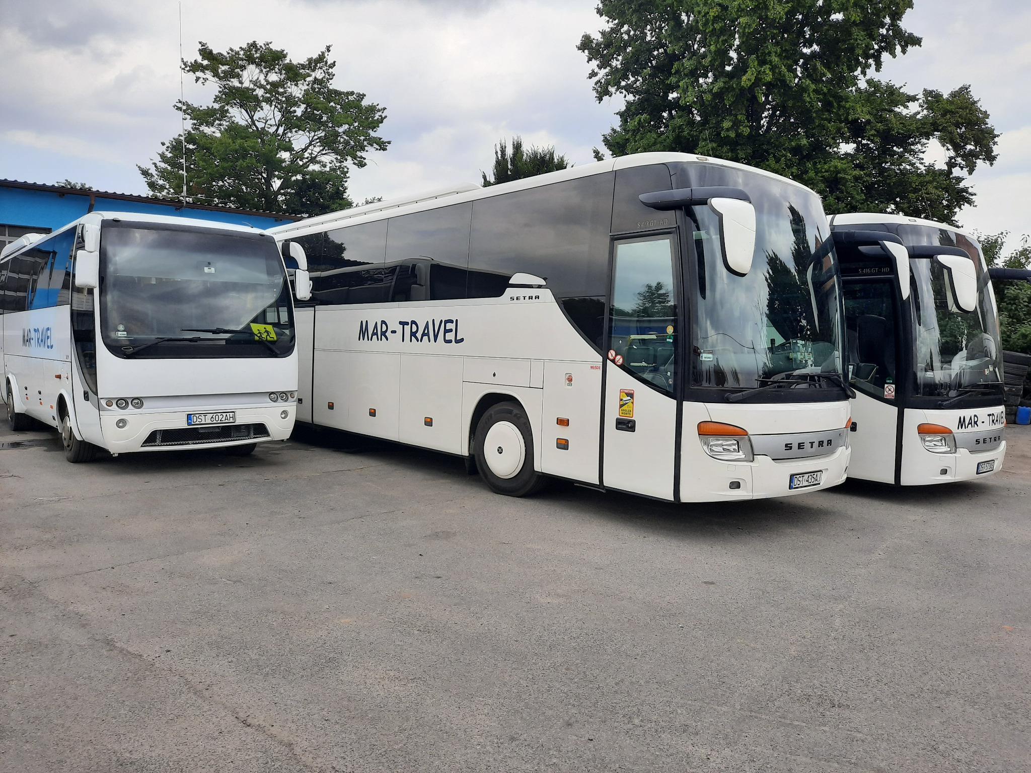 Trzy białe busy firmy Mar-Travel stojące obok siebie na parkingu, widok z przodu, z widocznymi numerami rejestracyjnymi.