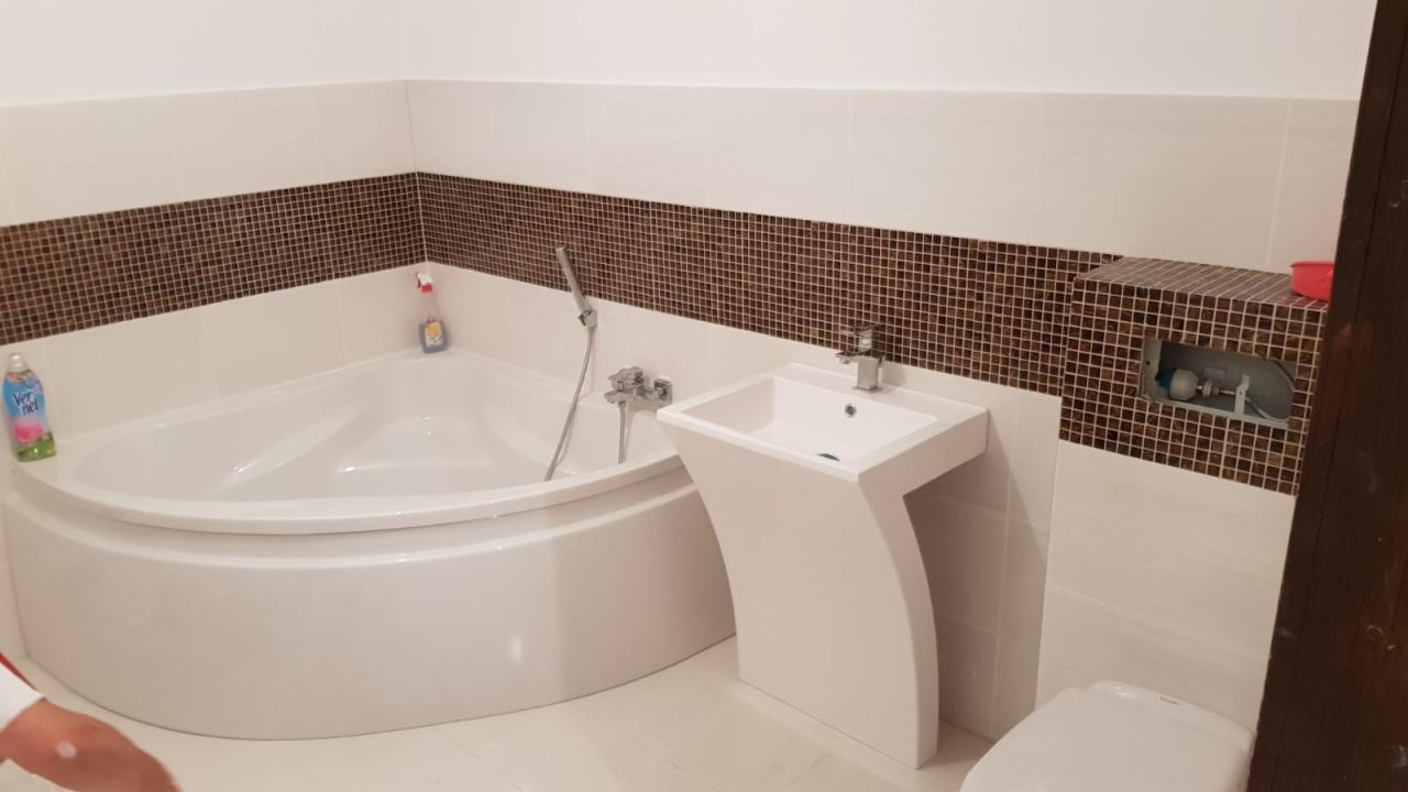 Nowoczesna łazienka z narożną wanną, umywalką na postumencie i mozaiką w odcieniach brązu na ścianach.