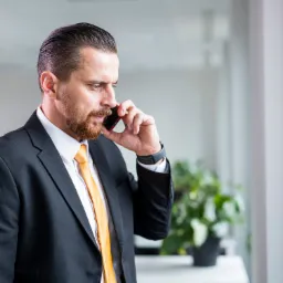 Mężczyzna w garniturze z pomarańczowym krawatem rozmawia przez telefon, zamyślony wyraz twarzy, widok z profilu.