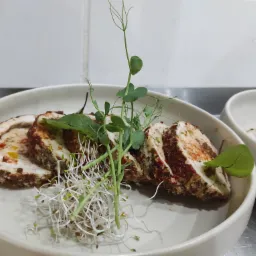 Rolada mięsna pokrojona w plastry, udekorowana świeżymi kiełkami i młodymi pędami groszku, podana na białym, głębokim talerzu.