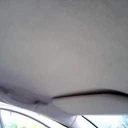 Wnętrze samochodu z widoczną podsufitką, uchwytem i osłoną przeciwsłoneczną, materiał o jasnoszarym odcieniu z delikatną teksturą.