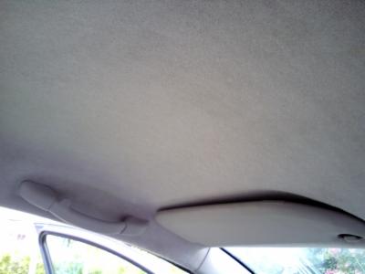 Wnętrze samochodu z widoczną podsufitką, uchwytem i osłoną przeciwsłoneczną, materiał o jasnoszarym odcieniu z delikatną teksturą.