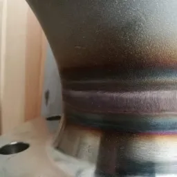 Spoina spawalnicza na metalowym kołnierzu, widoczne tęczowe przebarwienia po spawaniu.