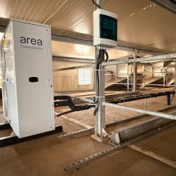 JAMRÓZ Nowoczesne Technologie - Biała jednostka klimatyzacji przemysłowej 'Area Cooling Solutions' w hali z metalową konstrukcją. Widoczne przewody i skrzynka elektryczna. Oświetlenie górne.