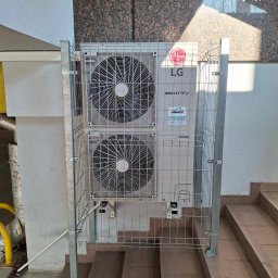 JAMRÓZ Nowoczesne Technologie - Zewnętrzna jednostka klimatyzacji LG Multi V zabezpieczona metalową klatką na schodach, z widoczną naklejką z danymi kontaktowymi firmy JAMROZ.