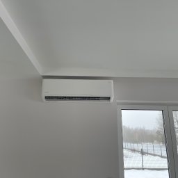 JAMRÓZ Nowoczesne Technologie - Biały klimatyzator Rotenso Neo, zamontowany na ścianie w jasnym pomieszczeniu z widokiem na zimowy krajobraz za oknem. Minimalistyczny design, nowoczesne wykończenie.