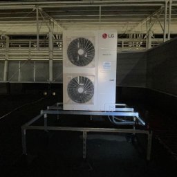 JAMRÓZ Nowoczesne Technologie - Biała jednostka zewnętrzna klimatyzacji LG Multi V, zamontowana na metalowej konstrukcji na dachu budynku, widoczna pod światłem reflektorów.