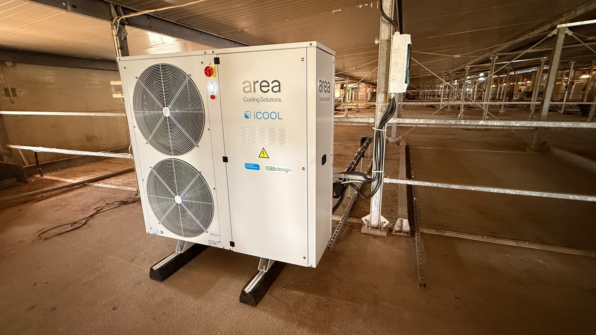 Biała jednostka klimatyzacyjna Area Cooling Solutions iCOOL z dwoma wentylatorami, zamontowana w hali produkcyjnej, widok z boku, kable zasilające.