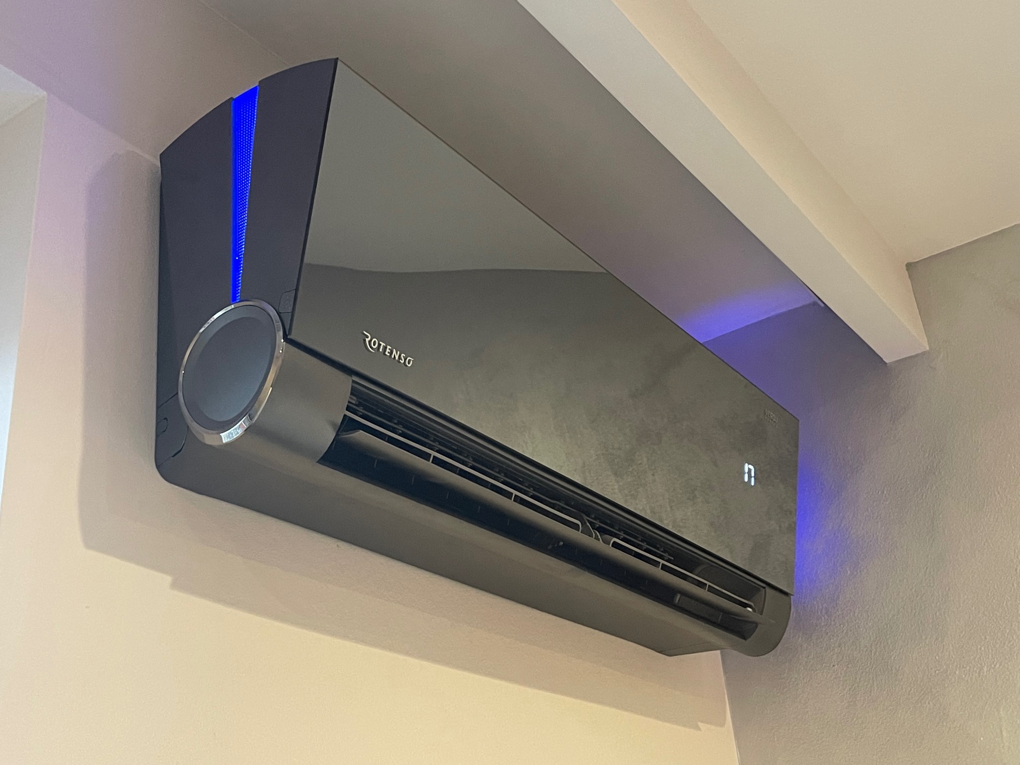 Czarna klimatyzacja Rotenso z niebieskim podświetleniem, zamontowana w pomieszczeniu w Pabianicach. Widoczny fragment sufitu i ściany.