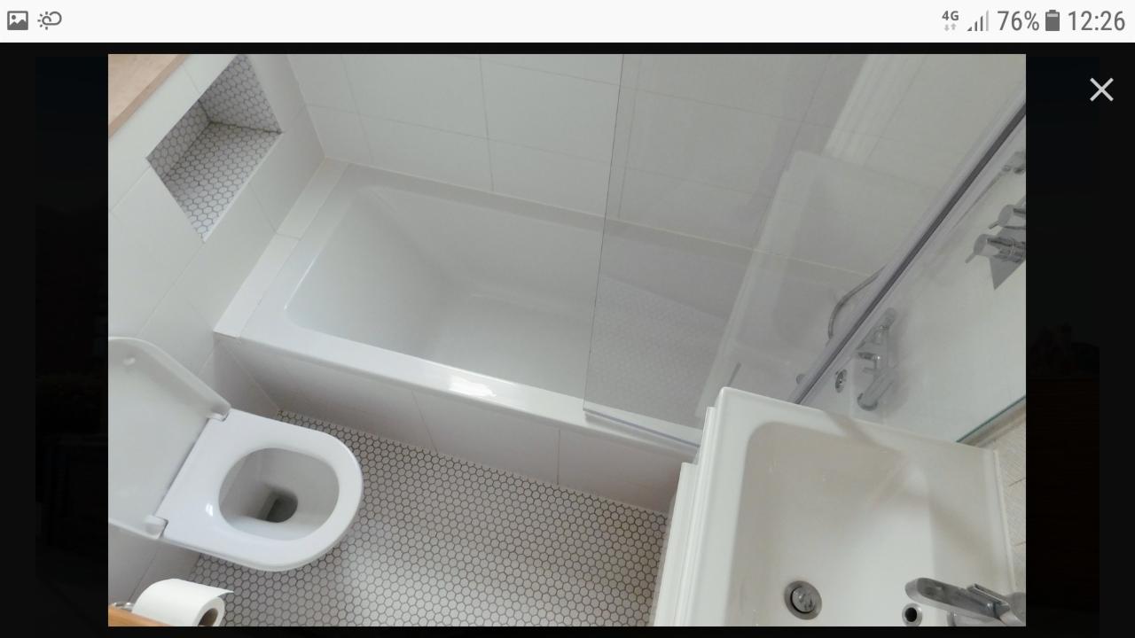 Biała łazienka po remoncie, widok z góry na wannę z parawanem, umywalkę, toaletę z otwartą klapą i mozaikową podłogę oraz wnękę ścienną wykończoną mozaiką.