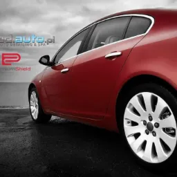 Czerwony samochód osobowy po detailingu, widoczne logo ad.auto.pl, Rupes BigFoot i PremiumShield na tle czarno-białego krajobrazu.