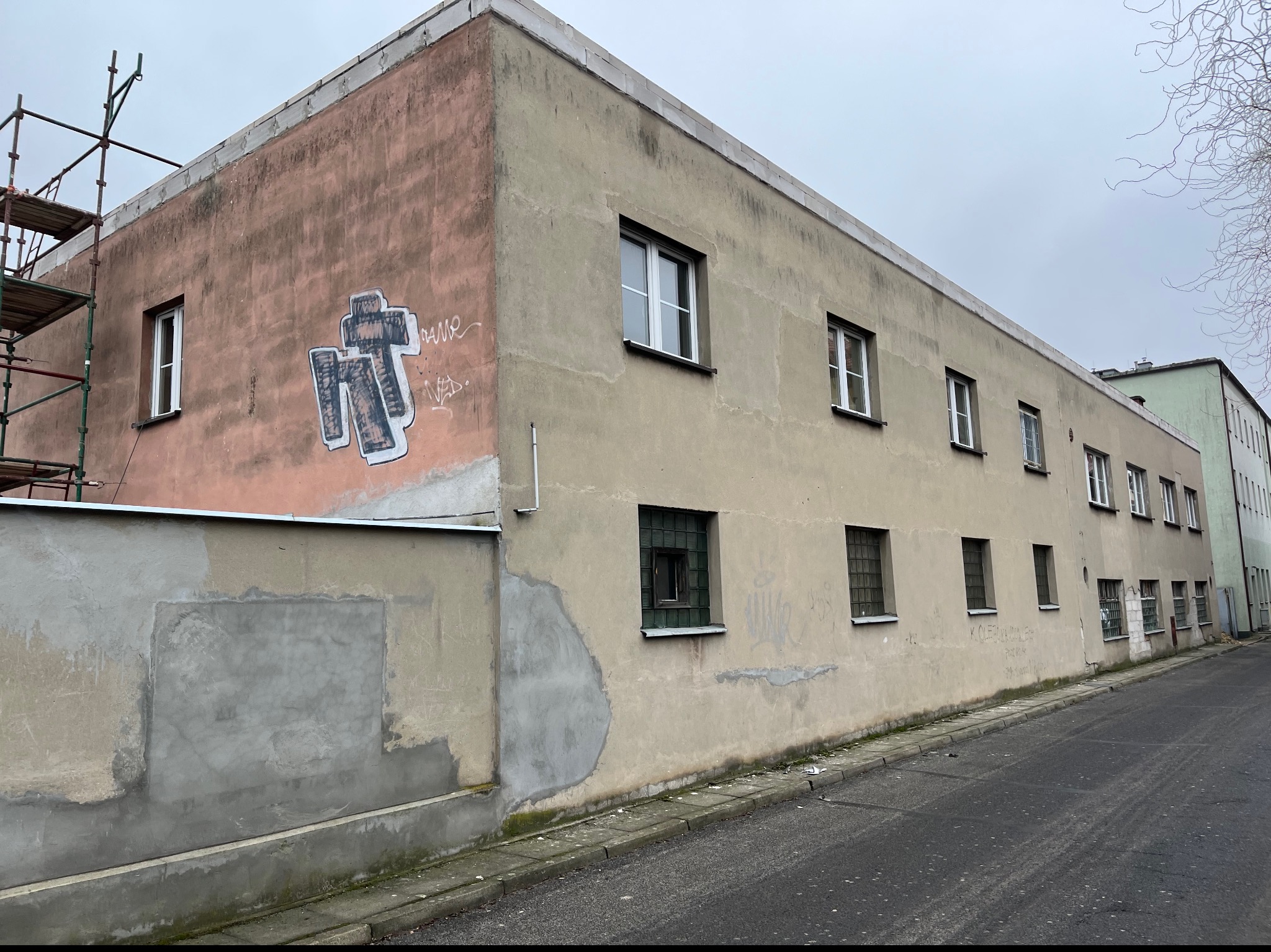 Budynek w Świętnie ze śladami napraw elewacji i graffiti, częściowo pokryty nowym tynkiem, widoczne rusztowania.