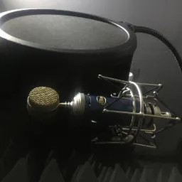 Mikrofon pojemnościowy Blue Yeti Pro z pop filtrem i ekranem akustycznym w ciemnym pomieszczeniu, widoczne detale siatki mikrofonu i srebrnego koszyka antywibracyjnego.