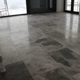 Ułożona szara marmurowa posadzka w nowym pomieszczeniu z dużymi oknami balkonowymi i widokiem na zaśnieżony krajobraz.