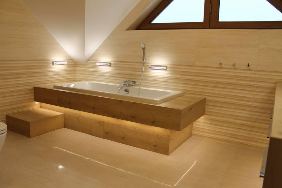 Nowoczesna łazienka na poddaszu z wanną obudowaną drewnem, podświetleniem LED i beżowymi płytkami z poziomym wzorem.