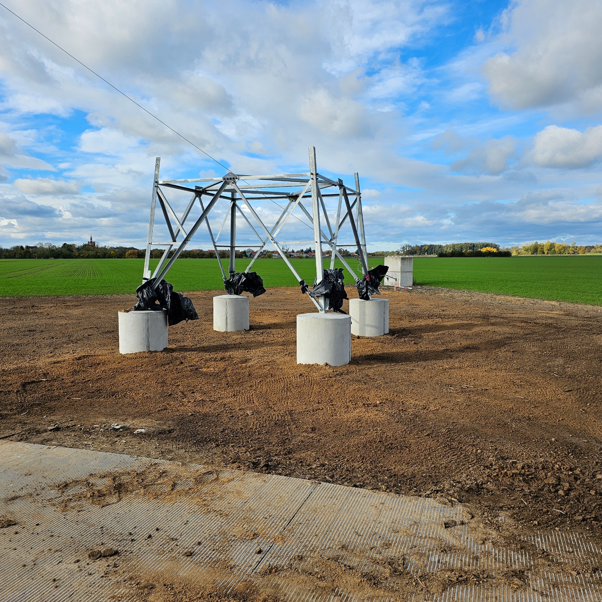 Konstrukcja stalowa na betonowych fundamentach na polu uprawnym pod błękitnym niebem z chmurami. Etap budowy domu szkieletowego.