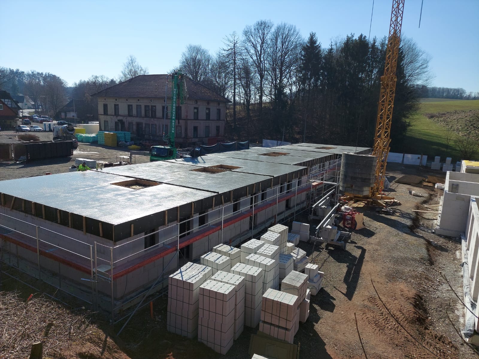 Budowa domu z keramzytu: ściany z pustaków, strop, rusztowania, żuraw. W tle budynek, drzewa i błękitne niebo. Widok z góry na plac budowy w słoneczny dzień.