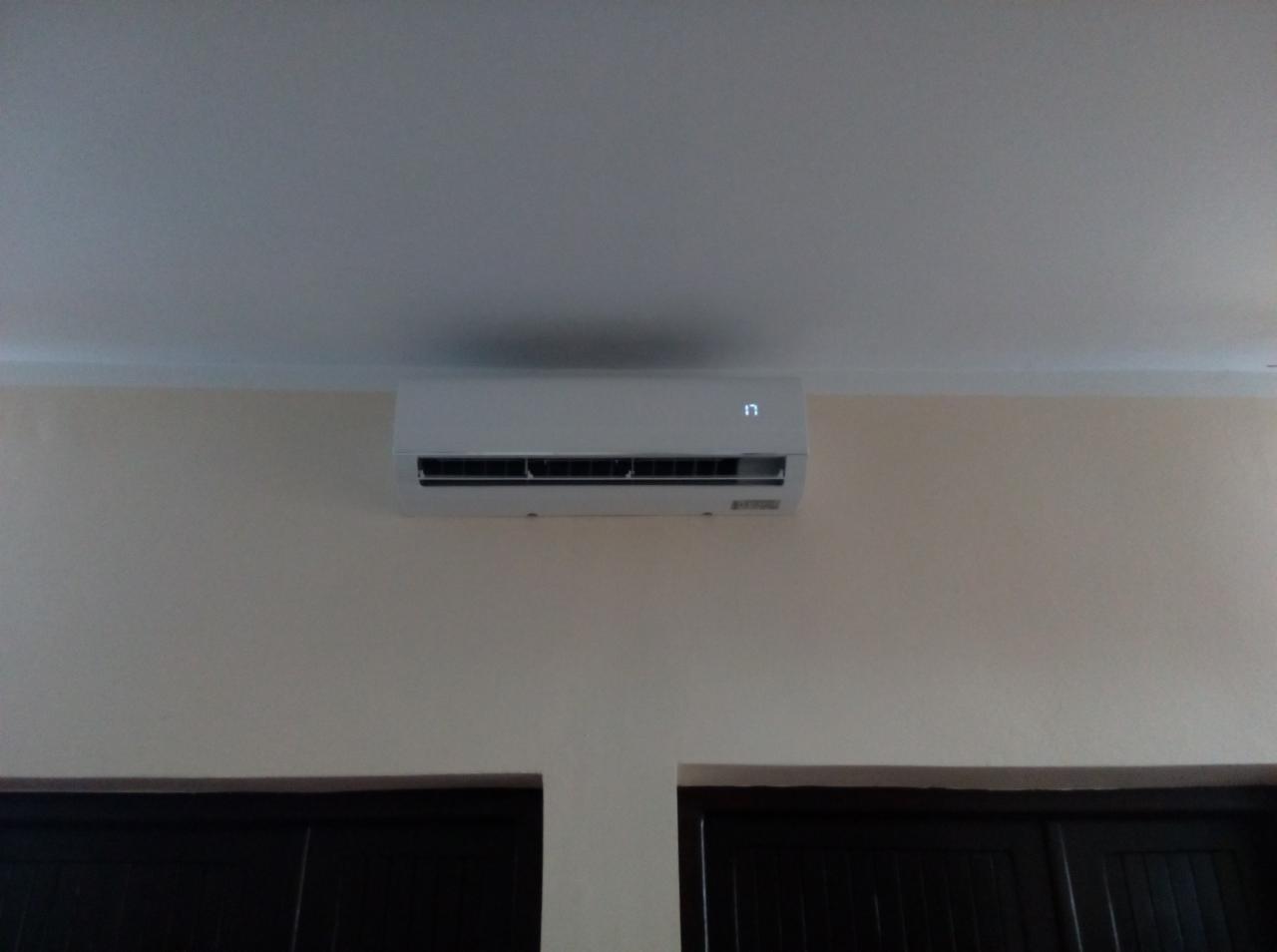 Biały klimatyzator ścienny zamontowany nad ciemnymi drzwiami, wyświetlający temperaturę 17 stopni Celsjusza na jasnej ścianie.