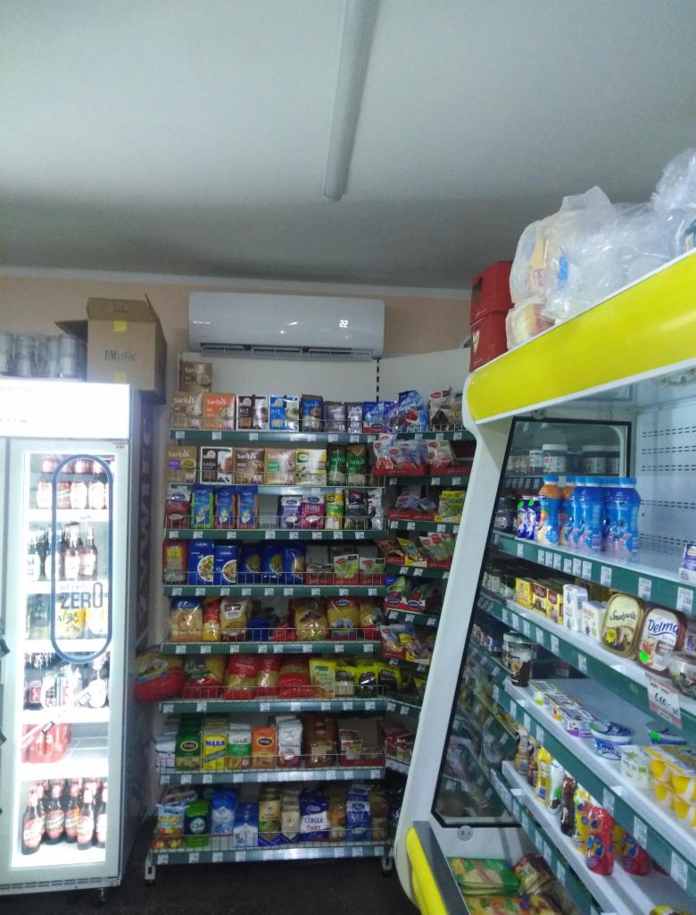 Klimatyzator ścienny zamontowany w sklepie spożywczym nad regałami z produktami.