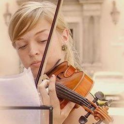 Dream come true s.r.o. - Młoda kobieta w plenerze gra na skrzypcach, skupiona na nutach, w tle architektoniczne detale budynku.