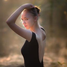 Dream come true s.r.o. - Młoda baletnica w czarnym stroju z odkrytymi plecami, pozująca w zalesionym otoczeniu, oświetlona ciepłym, rozproszonym światłem.
