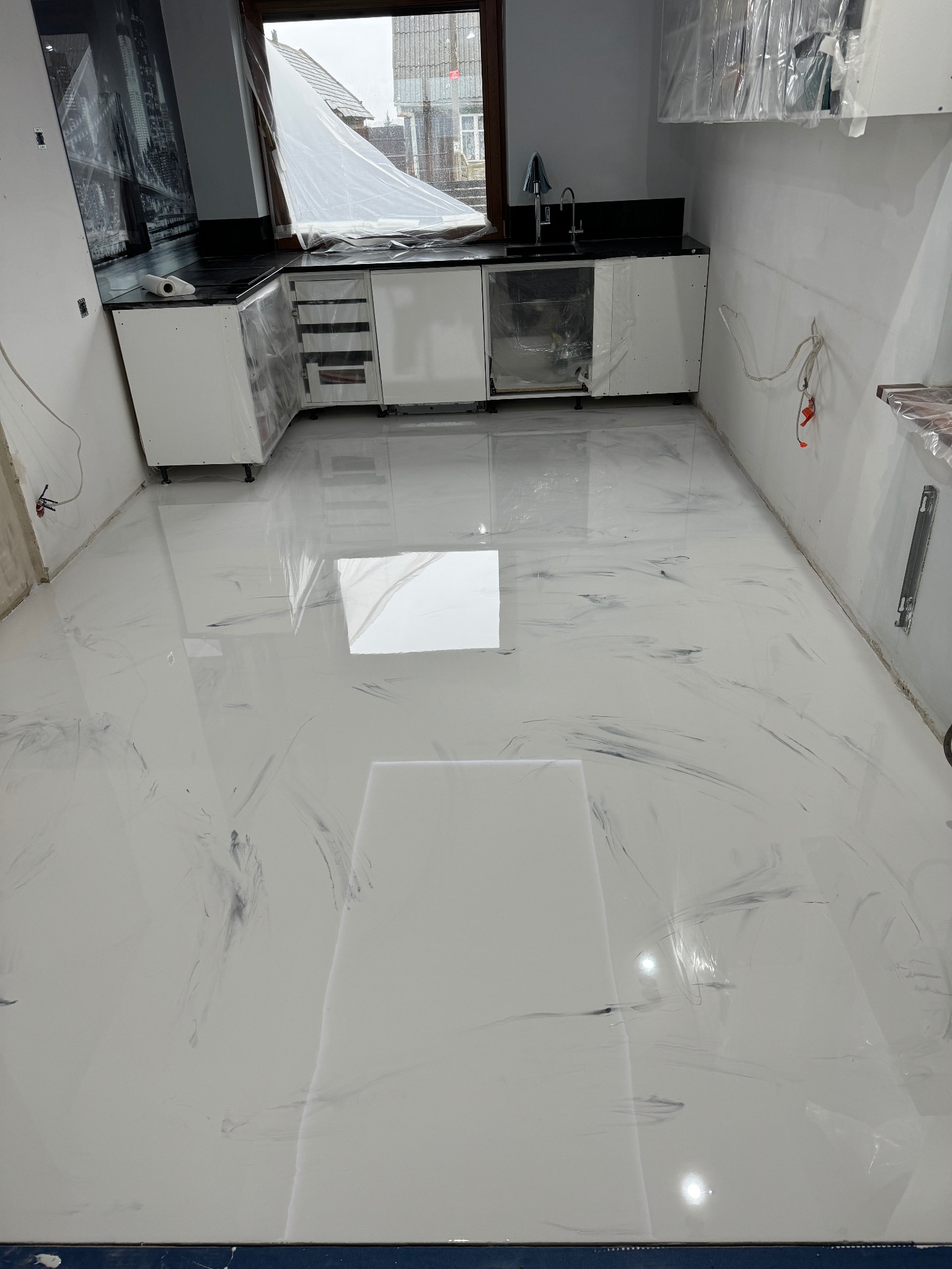Biała podłoga z szarymi żyłkami w nowo wykończonej kuchni, meble kuchenne zabezpieczone folią ochronną.