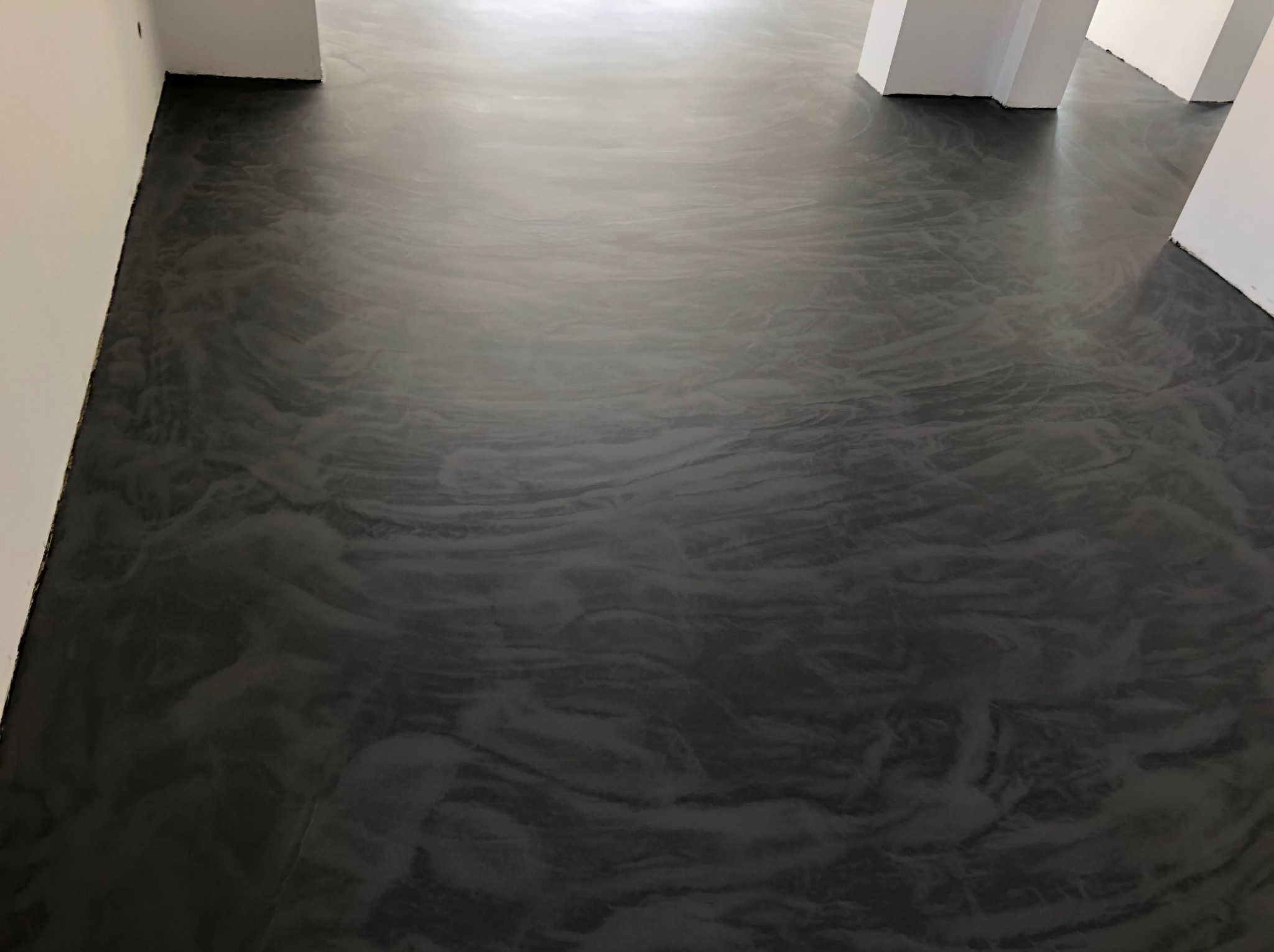 Błyszcząca, ciemnoszara posadzka żywiczna z marmurkowym wzorem w nowym pomieszczeniu z białymi ścianami i kolumnami.