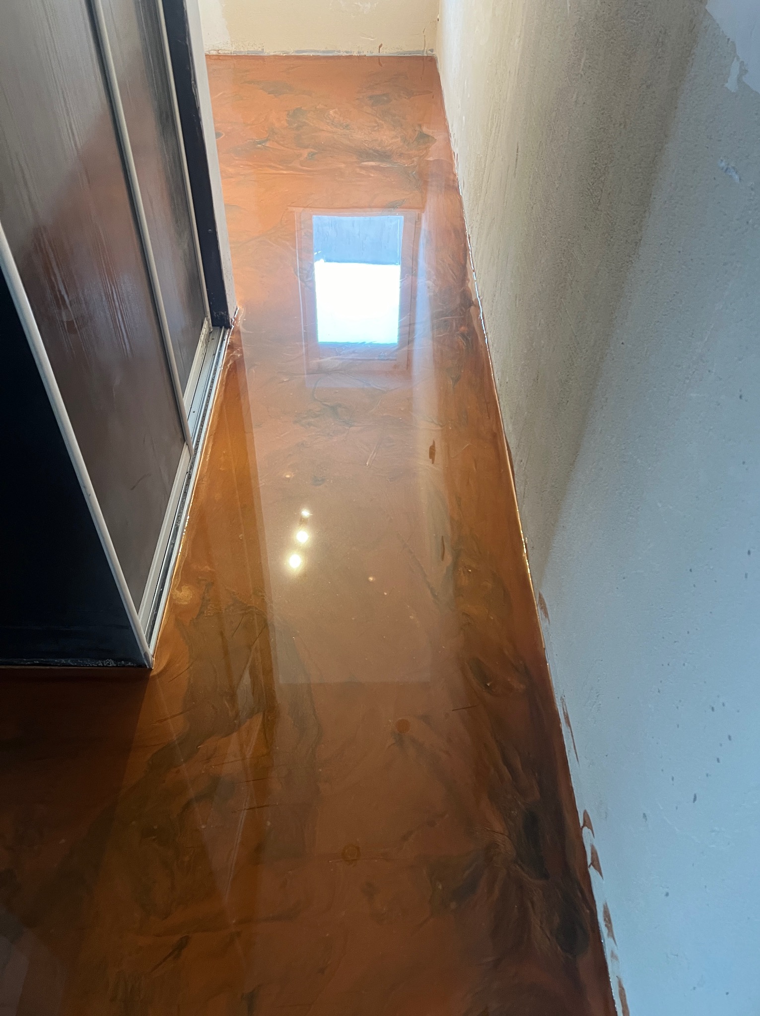 Błyszcząca, brązowa podłoga z efektem marmuru w niedokończonym pomieszczeniu, widoczne surowe ściany i przesuwne drzwi.