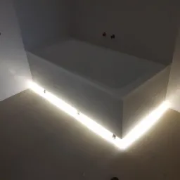 Biała wanna z podświetleniem LED u dołu, zamontowana w łazience z jasnymi płytkami i grzejnikiem drabinkowym na ścianie.