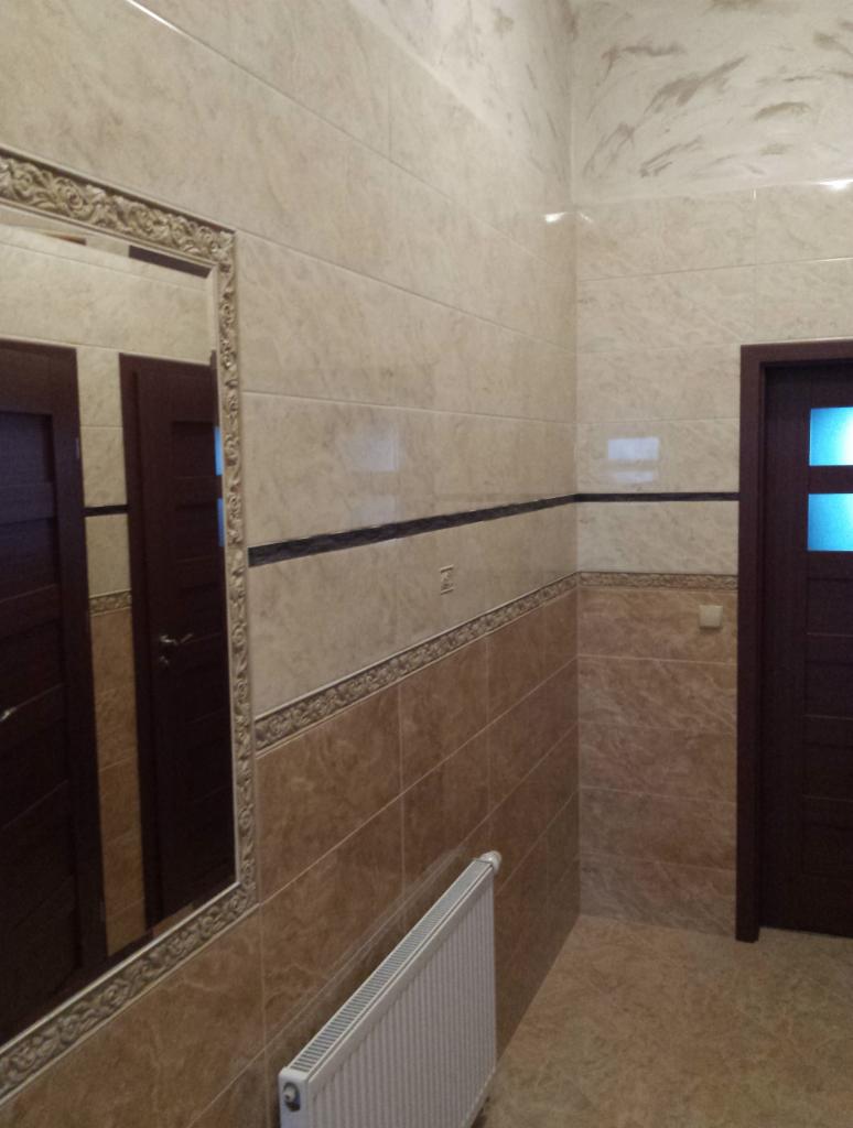 Wykończona łazienka z beżowymi i brązowymi płytkami, dekoracyjnym lustrem i grzejnikiem na ścianie.