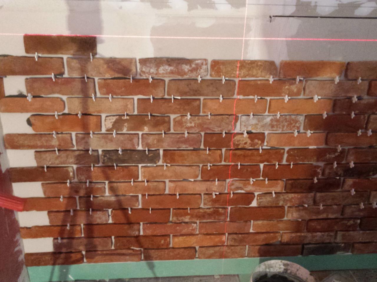 Murowanie ściany dekoracyjnej z cegieł klinkierowych, widoczne krzyżyki dystansowe i poziomica laserowa.