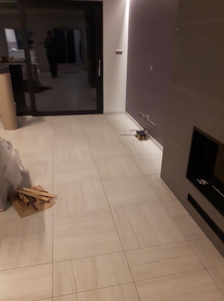 Wnętrze po odświeżeniu w Krzywiniu: kremowe płytki podłogowe z delikatnym wzorem, fioletowa ściana z listwą LED, przesuwne drzwi balkonowe i karton z drewnianymi listwami przy ścianie.