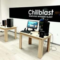 Ekspozycja stanowisk komputerowych wysokiej klasy marki Chillblast w salonie, z komputerem stacjonarnym, monitorem, klawiaturą, myszą, kontrolerami i zestawem VR na drewnianym stole.