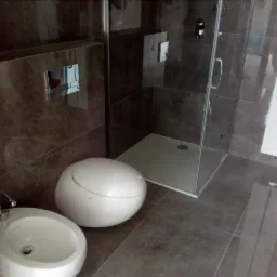 Nowoczesna łazienka z brązowymi płytkami: kabina prysznicowa z odpływem liniowym, okrągła umywalka z baterią i kulisty bidet.